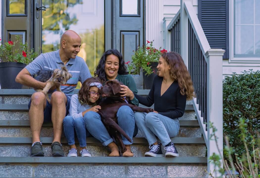 young family and puppy sitting on front porch steps 